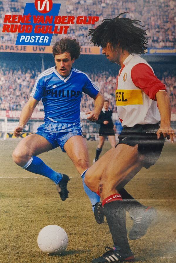 Voetbalwedstrijd met twee spelers in actie, één in blauw en één in rood, op een stadionveld tijdens.