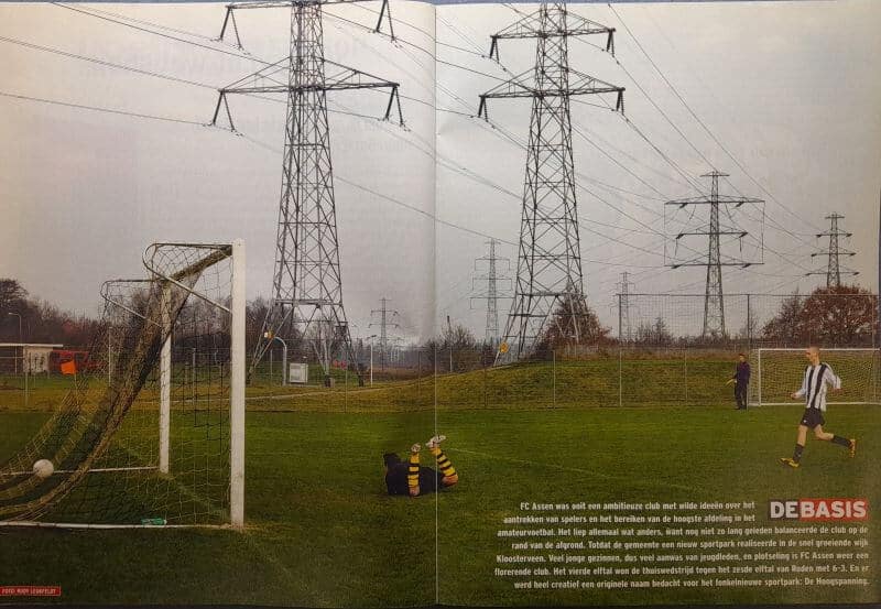 Voetbalveld met hoogspanningsmasten en spelers in actie.