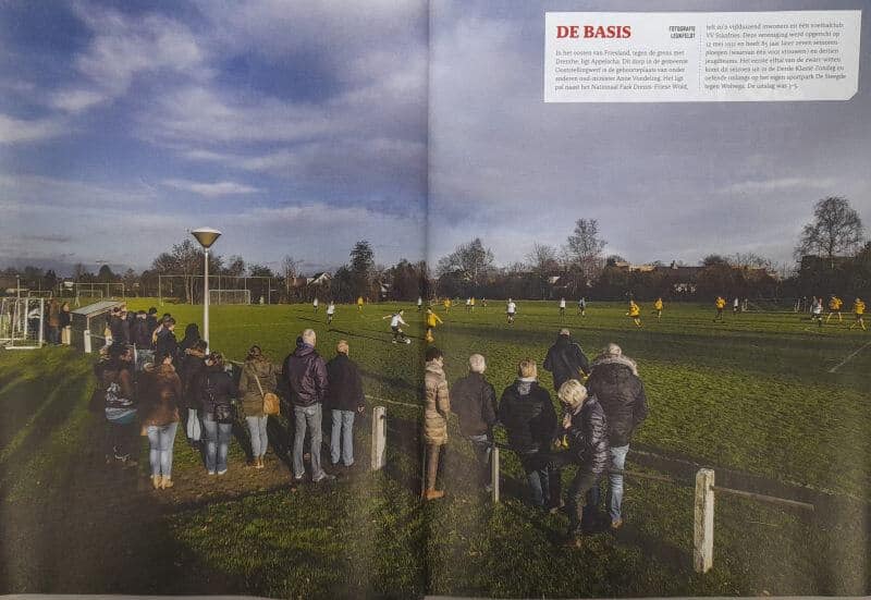 Publiek kijkt naar een amateurvoetbalwedstrijd op een grasveld in Friesland.
